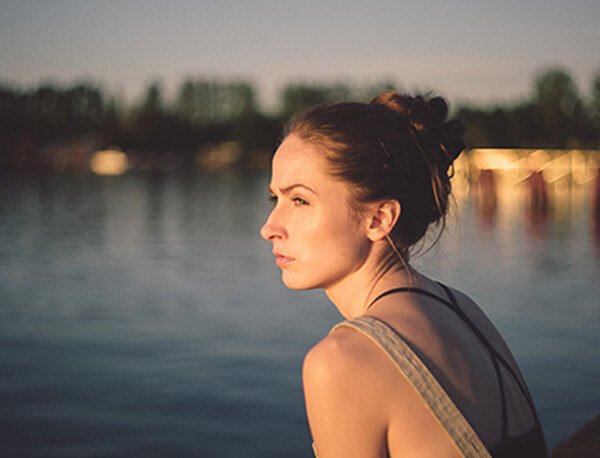 A woman sits by the waterside gazing contemplatively.