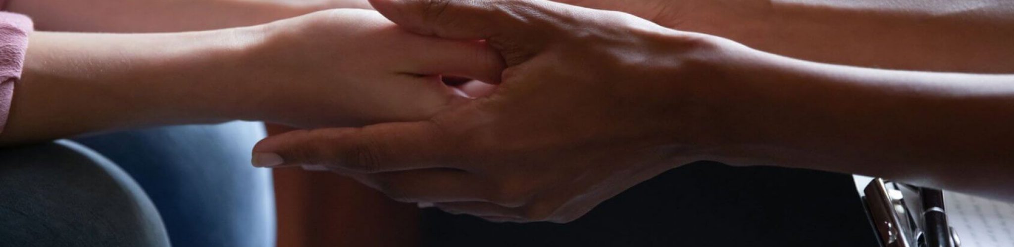 A closeup of two women's hands reaching out and clasped together.